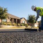 Chip-seal crew applying new aggregate to a Texas driveway, showing textured surface and compact roller.