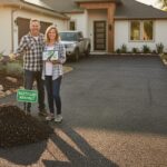 A couple standing on a freshly paved recycled asphalt driveway in front of their modern Texas home, showcasing eco-friendly driveway materials.