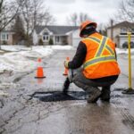 Worker applying cold patch to pothole on wet asphalt driveway during spring thaw